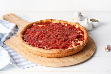 Board with tasty Chicago-style pizza, garlic and spices on light wooden background