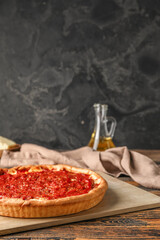 Board with tasty Chicago-style pizza on dark background