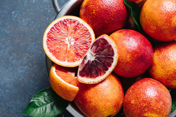 Whole and sliced blood oranges in iron bowl colander on blue table background. Flat lay, top view,...