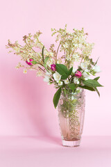 Bouquet of meadowsweet (Latin Filipndula), jasmine and wild roses in a vase on a pink background.