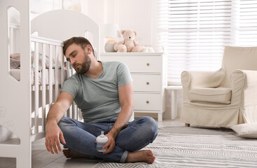 Tired father with bottle of milk sleeping on floor in children's room