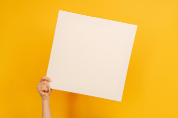 Woman hand holding white canvas paper blank with copyspace on yellow background. Empty sheet banner...