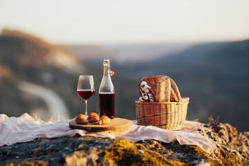 Romantic picnic with basket with baguette, red wine and croissants in the mountain at sunny day. - obrazy, fototapety, plakaty
