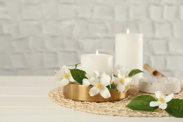 Beautiful jasmine flowers and burning candles on white wooden table, space for text