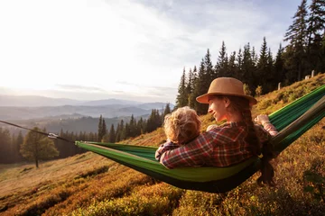 Poster Boy with mom resting in a hammock in the mountains at sunset © Maygutyak