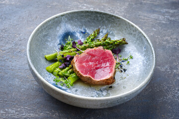 Modern style traditional green asparagus with fried dry aged sliced beef fillet steak and green asparagus served as close-up on a Nordic design plate
