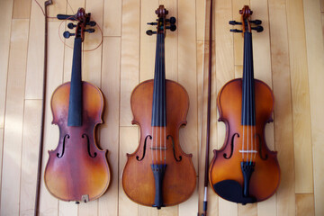 Fototapeta na wymiar three brown violins music instruments on wood floor background