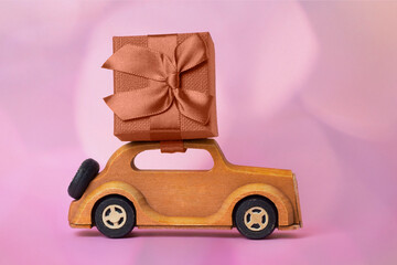 Fototapeta premium Wooden car with a gift on a pink background.
