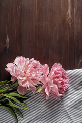 floral vertical banner. pink peony flowers bouquet on a kitchen towel on a dark wooden background. simple flat composition with place for text. flat lay, copy space