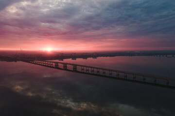 Fototapeta na wymiar Aerial drone filmed sunset, burning sky over the city and water, beautiful sunset or sunrise. Panoramic view over the bridge with the sun