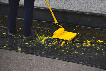 Man painting a wall in yellow colour. Paint roller in a paint tray near a grey wall. Black plastic cover on the ground.