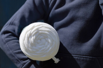 A bobbin of white cotton cord in the hands of a child on a blue background.