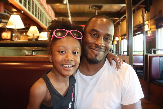 Black Man and little girl customers smiling close up  wearing summer closthing sitting indoors in restaurant booth