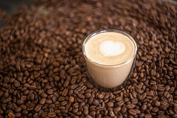 Coffee. Glass cup with cappuccino with latte art stands on coffee beans.
