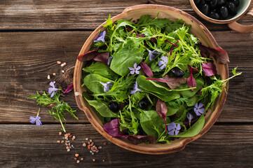 Asian salad mix with baby spinach, mizuna salad, edible flowers and olives on wooden background,...