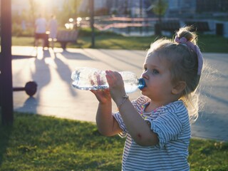 
little girl drinks water from a plastic bottle on a walk in the park