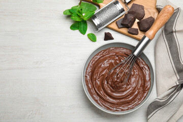 Chocolate cream with balloon whisk and mint on white wooden table, flat lay. Space for text
