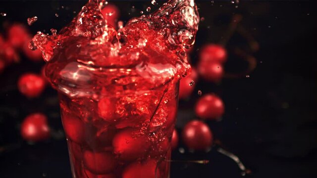 Super slow motion in a glass of juice drops cherry with splashes. On a black background. Filmed on a high-speed camera at 1000 fps.