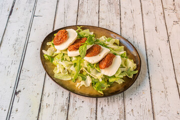 Caprese salad with dehydrated tomato preserved in olive oil, buffalo cheese slices, lettuce and arugula on a beautiful brown plate