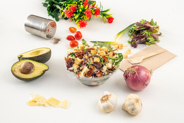 Plastic bowl for home delivery with Cesar salad of croutons, battered chicken, sprouts of assorted vegetables, cherry tomatoes, onion, avocado and garlic on white background
