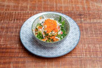 Wakame seaweed salad with crumbled surimi and orange fish roe on a beautiful plate in blue tones and wooden table