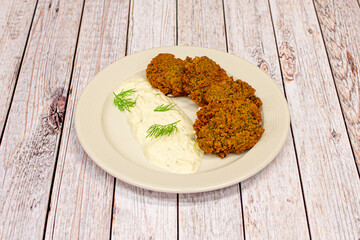 Greek plate of falafel balls with vegetables and sauce on white plate