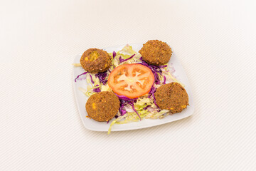 Falafel balls mixed with lettuce, purple cabbage and tomato salad on small white plate
