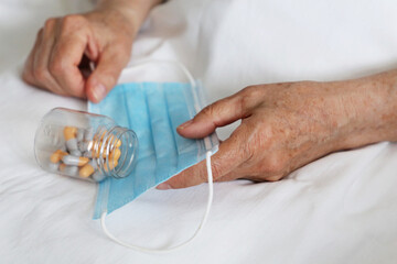 Elderly woman with pills in wrinkled hands on medical mask. Taking medication in capsules during coronavirus pandemic