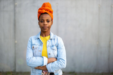 Young woman wearing orange headscarf in front of gray wall 
