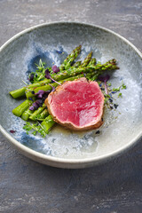 Modern style traditional green asparagus with fried dry aged sliced beef fillet steak and green asparagus served as close-up on a Nordic design plate