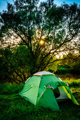 green tourist tent by the river at sunset