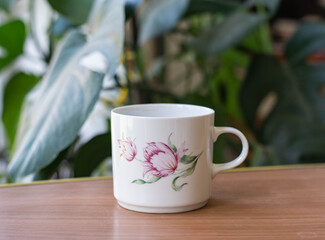 Vintage porcelain cup with tulip pattern on a wooden table with plants on the background