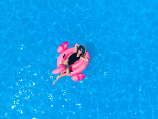 Woman on flamingo pool float in pool in hotel. Summer holidays, enjoying summer vacations during quarantine.