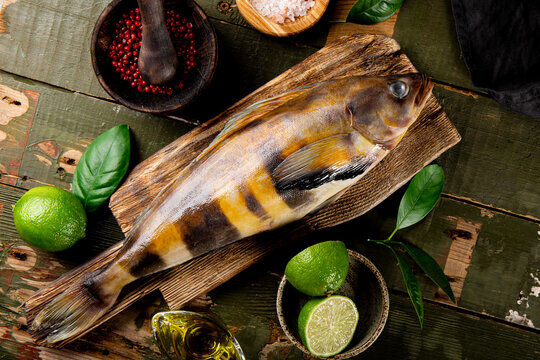  Raw fish sea bass or lingcod and seasonings for cooking it on an old plank background top view