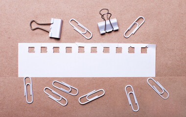 On a brown background, white paper clips and a torn strip of white paper with space to insert text....