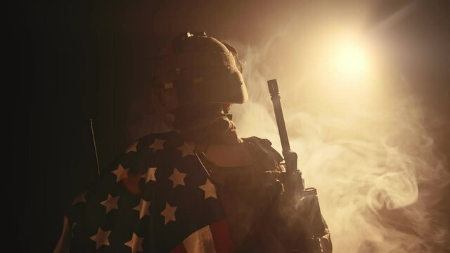 soldier standing with his back to us in the dark holding USA national flag