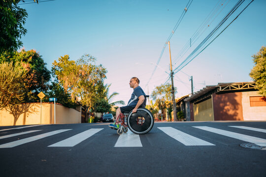 Latino man using wheelchair on street crossing the crosswalk.