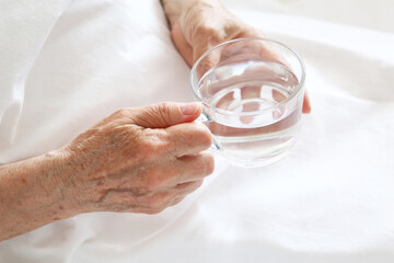 Elderly woman with glass of clean water in wrinkled hands. Concept of thirst, diet at retired,...