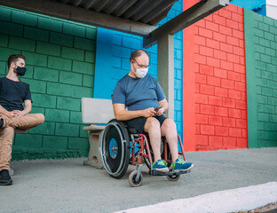 Latino man using wheelchair on bus stop using smartphone.