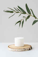 White plastic jar for branding on wooden podium and eucalyptus branch with green leaves on grey background. Natural beauty and spa product presentation. Empty cream box mockup. Cosmetic advertising.