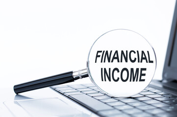 Financial Income text on a magnifying glass that stands on the keyboard of a laptop on a white background