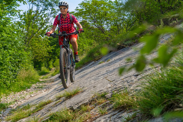 Fototapeta na wymiar nice, active senior woman riding her electric mountain bike in the huge rock fall area of Marocche di Dro, in the Sarca Valley, Garda lake mountains, Trentino, Italy 