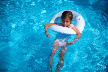 Happy little girl swims and plays in the pool. Summer vacation.