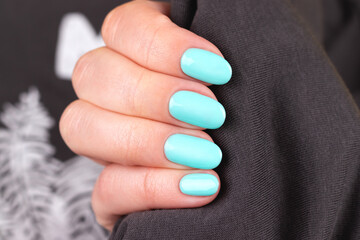 Female hand with beautiful manicure - turquoise, mint blue nails on gray textile fabric background, closeup. Nail care concept