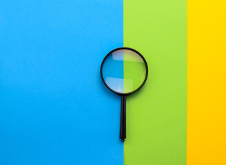 Magnifying glass on multi-colored paper. Top view. Copy space for text.