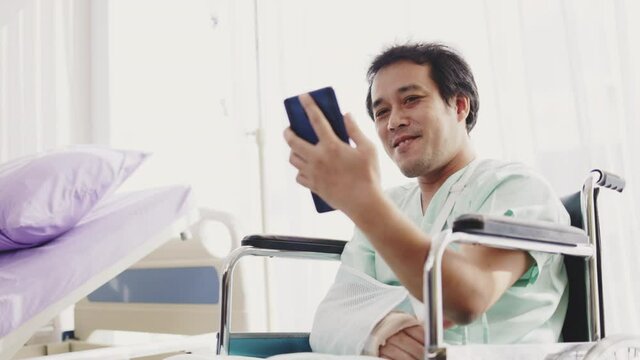 Asian man patient splint on arm using smartphone for video call Consult an orthopedic doctor Sit in wheelchair the hospital room. Service Medical consult. tele health and telemedicine concept.
