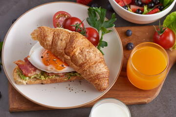 Delicious breakfast with fresh croissants, bacon sandwich with fried egg. milk served, orange juice. strawberry, butterhead, blackberry salad. full american healthy breakfast top view.