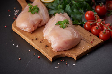 raw chicken fillet with garlic, pepper and rosemary on wooden on chopping board. fresh fillet. fresh chicken meat, chicken fillet with spices at black stone table. top view with copy space..
