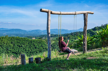Asian fat guy sitting on wooden swing with Beautiful landscape view on Phu Lamduan at loei thailand.Phu Lamduan is a new tourist attraction and viewpoint of mekong river between thailand and loas.