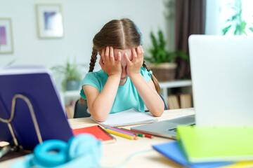 little girl is tired of learning. home schooling, homework. girl rubs his eyes from fatigue reading...